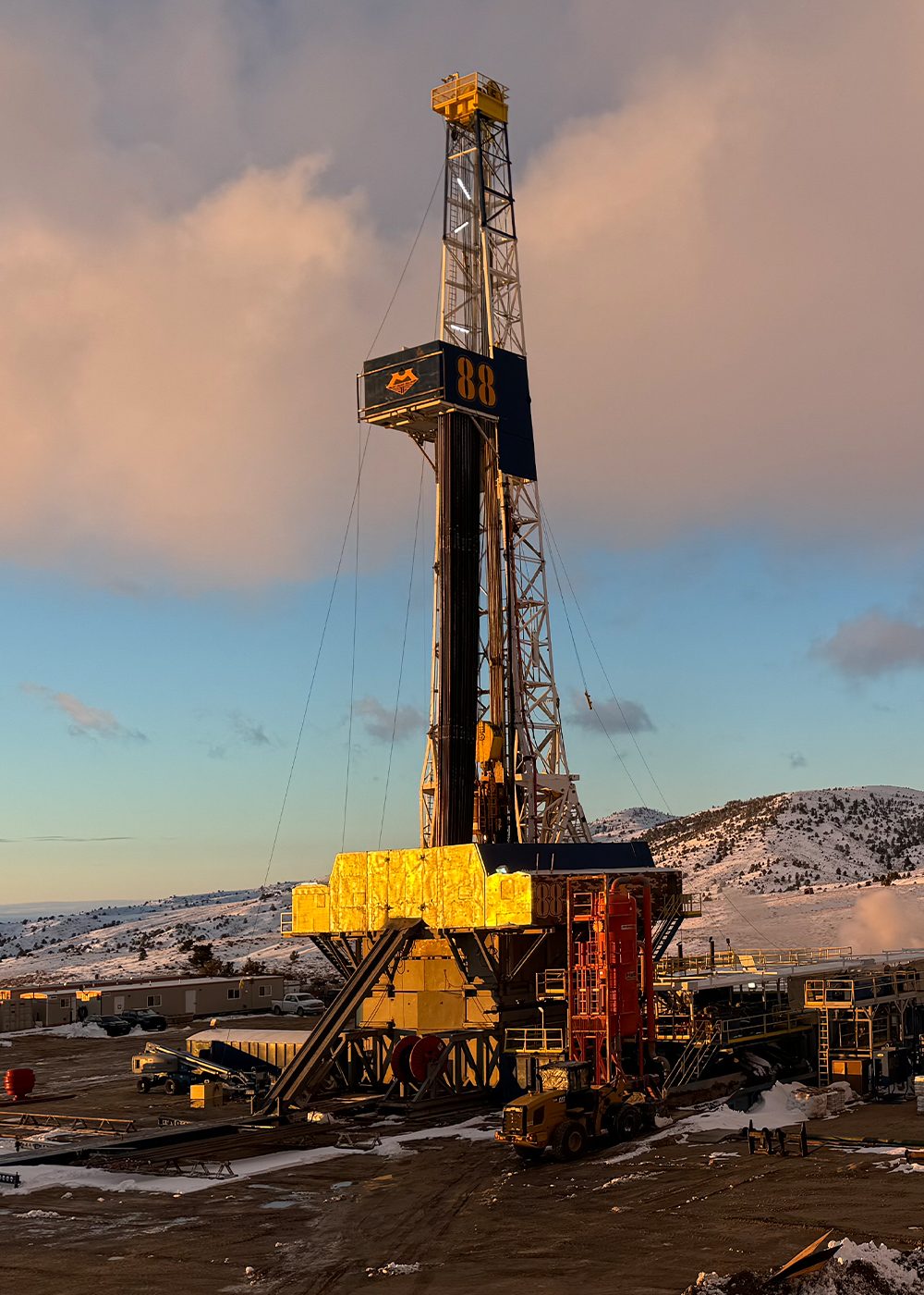 Oil and gas drilling rig set against a snowy mountain backdrop at sunset